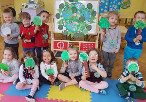 zdjęcie zbiorowe - dzieci prezentują wspólną pracę „Nasza planeta Ziemia”, drzewa z rolek po papierze toaletowym oraz medale pamiątkowe z obchodów Dnia Ziemi.
